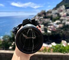 Camera and broken lens in hand with view over Positano town and beach in Amalfi coast in Italy. photo