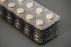 Multiple rows of pill blisters stacked on a gray surface in a close-up view photo