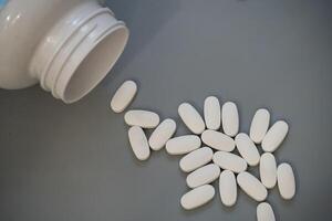 Bottled white tablets scattered on a gray surface after spilling photo