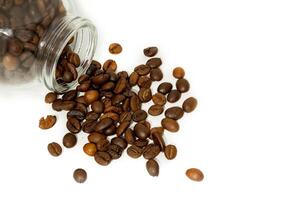 Coffee beans spilling from a glass jar on a white surface photo
