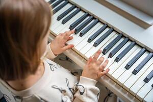 Home lesson on music for the girl on white piano synthesizer. Concept of early development. learning music enhances motor skills, hearing, and intelligence, fostering creativity from childhood. photo