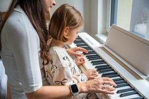 Home lesson with teacher on music for girl on white piano synthesizer. Concept of early development. learning music enhances motor skills, hearing, intelligence, fostering creativity from childhood. photo
