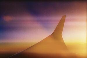 View of an airplane in flight during sunset, with the wing in the foreground photo