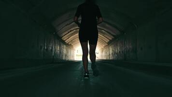 woman running in a dark tunnel to meet the light. Silhouette of a woman from behind running to the light. video