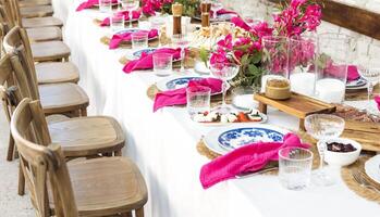 A set festive table in the open air. The table is decorated with candles and flowers. Delicious snacks, empty plates, glasses and raspberry napkins. photo