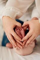 A close up of parents hands forming a heart around their newborns tiny feet, symbolizing love, family, and new beginnings. photo