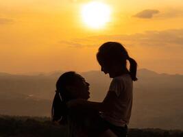 Silhouette of a daughter hugging and kissing her mother with love. Happy family mother and daughter in the park at sunset. photo