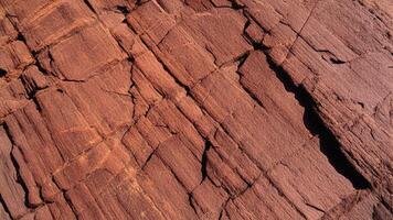 Cracked red rock face with pronounced crevices and rough textures, representing geological beauty suitable for architectural design, backgrounds, and organic pattern projects. photo