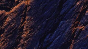 Dark rugged rock texture with deep blue shadows and rich earthy tones, showcasing natural geological patterns ideal for abstract backgrounds, architectural surfaces, and organic design inspirations. photo