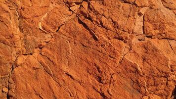 Bold orange rock texture with layered sediment patterns and natural fissures, ideal for geological design, architectural backgrounds, and organic surface inspirations. photo