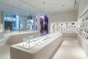 Bright and spacious retail environment features multiple displays of innovative gadgets, arranged neatly on white surfaces. Soft lighting highlights the sleek design and modern technology. photo