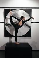 Full length beautiful gymnast in black suit is posing on black podium in backlight. The grace, artist, movement, action and motion concept. Looks weightless, flexible. How art become action. Vertical photo