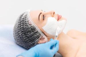 Caucasian middle-aged woman receiving a moisturizing facial mask applied by a beautician in a spa setting. Relaxing facial treatment at a spa for glowing skin rejuvenation photo