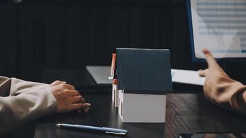 Two people sitting at a table with a house model video