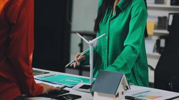 A woman is standing at a desk with a wind turbine video