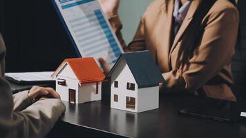 A woman is holding a house model and a man is looking at it video
