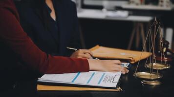 A lawyer and a client are sitting at a desk with a scale and a paper video