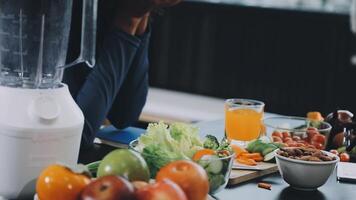 A woman sitting at a table with a blender and a bowl of fruit and vegetables video
