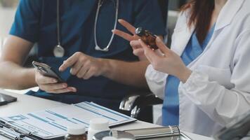 A doctor and a nurse are sitting at a desk with a tablet and a phone video