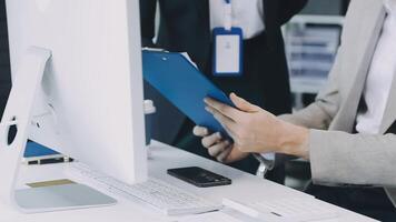 A man in a suit holding a clipboard while looking at a computer video