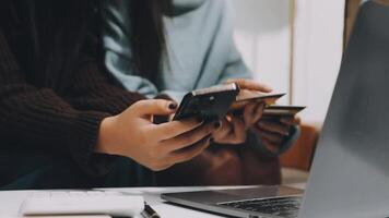 Two women using their phones while sitting at a table with a laptop video