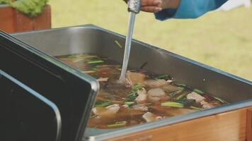 A person is stirring a pot of soup in a large metal container video