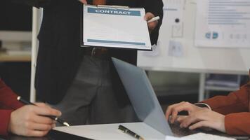 A man is holding a contract while two other people look on video