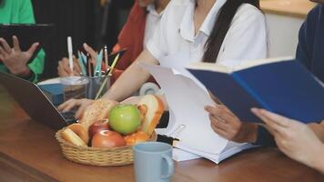 A group of people sitting at a table with laptops and books video