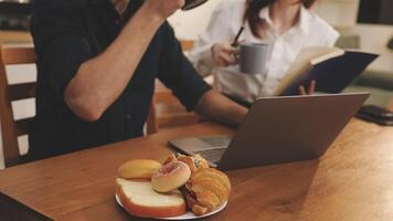 A man and woman sitting at a table with a laptop and croissants video