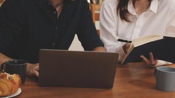 A man and woman sitting at a table with a laptop and a book video