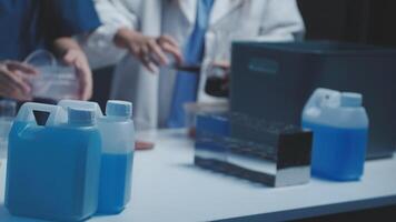 Two people in lab coats are working on a table with blue liquid video