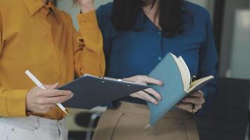 Two women are holding notebooks and looking at a computer video