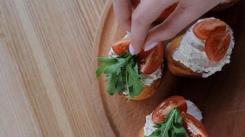 Adding arugula to tomato-topped bruschetta, Hand placing fresh arugula on bruschetta with tomato and cream cheese. video