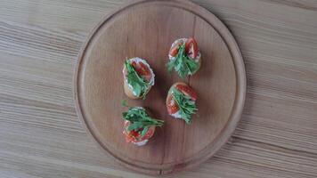 Fresh bruschetta with tomatoes and arugula on a wooden plate, A hand arranging bruschetta topped with tomatoes and arugula. video
