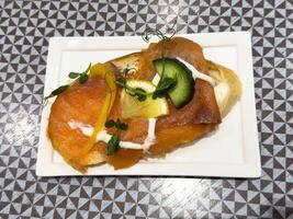Smoked salmon on rustic toast with cucumber and lemon garnish on geometric patterned table photo