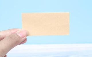 Hand holding a blank piece of paper on a blue background. Blank sheet for writing text on palm. Free space for text and ads photo