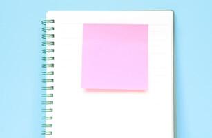 Pink sticky note on a notebook isolated with blue background. Journaling and office desk concept with copy space photo