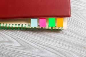 Four colored markers with notebooks on a wooden table. Colorful sticky note bookmarks were attached to two notebooks. Journaling and office desk concept photo