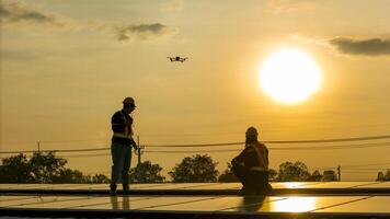 Silhouette of workers ins talling solar panels on a rooftop during sunset with a drone hovering nearby, highlighting renewable energy, innovation, and sustainable practices in solar technology. photo
