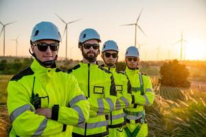 Wind energy technicians pose confidently at sunset in front of wind turbines in a rural setting photo
