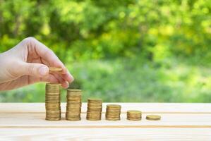 Business concept. A hand lays a coin on a column of coins on a wooden table with a green bokeh background. Success and business growth. The accumulation of money. Copy space. photo