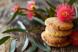 Stack of delicious anzac biscuits resting on rustic wood with eucalyptus leaves and flowers photo