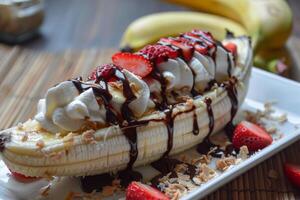 Banana split drizzled with chocolate sauce on white rectangular plate photo