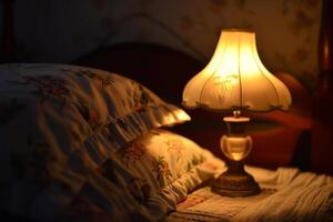 Vintage table lamp illuminating floral pillows in a dark bedroom photo