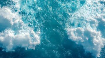 Ocean wake pattern stretches behind cruise ship in aerial view. Deep blue sea meets bright sky with white clouds, while turquoise foam trails create dynamic water movement on sunny day. water photo