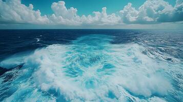 Ocean wake pattern stretches behind cruise ship in aerial view. Deep blue sea meets bright sky with white clouds, while turquoise foam trails create dynamic water movement on sunny day. nautical photo