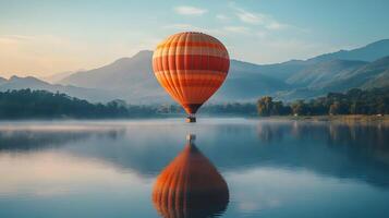 Hot air balloon floating above a mountain lake at dawn, capturing perfect reflection in calm waters with pastel sunrise colors and dreamy morning mist in a panoramic view. mountain photo