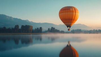 Hot air balloon floating above a mountain lake at dawn, capturing perfect reflection in calm waters with pastel sunrise colors and dreamy morning mist in a panoramic view. water photo