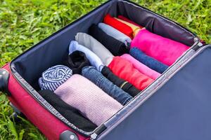 Open suitcase on the grass with different clothes folded vertically. Vertical storage for easy travel packing. photo
