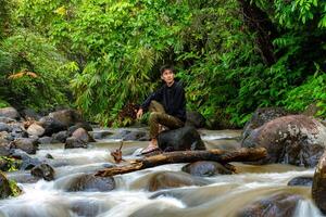 Man sitting on the river while looking around. Lonely man sitting on the rocks photo